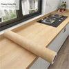 Roll of self-adhesive wood grain waterproof wallpaper next to a window with a dark countertop.