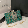 Emerald green rhinestone evening clutch with gold chain strap displayed on a black box.