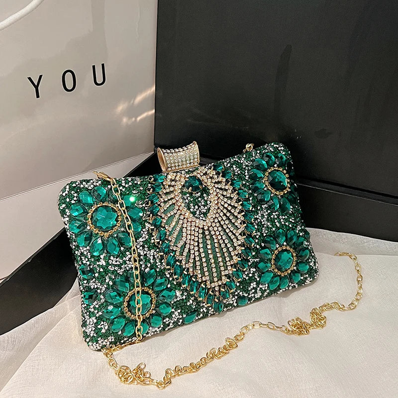 Emerald green rhinestone evening clutch with gold chain strap displayed on a black box.
