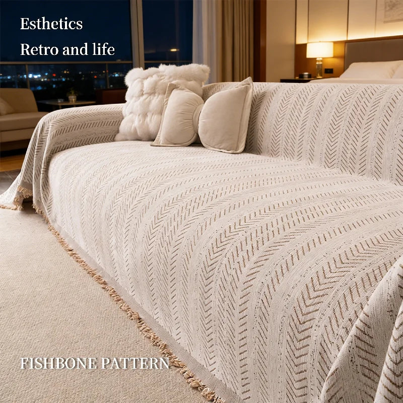 A close-up of a beige knitted throw blanket featuring a fishbone pattern draped over a bed.