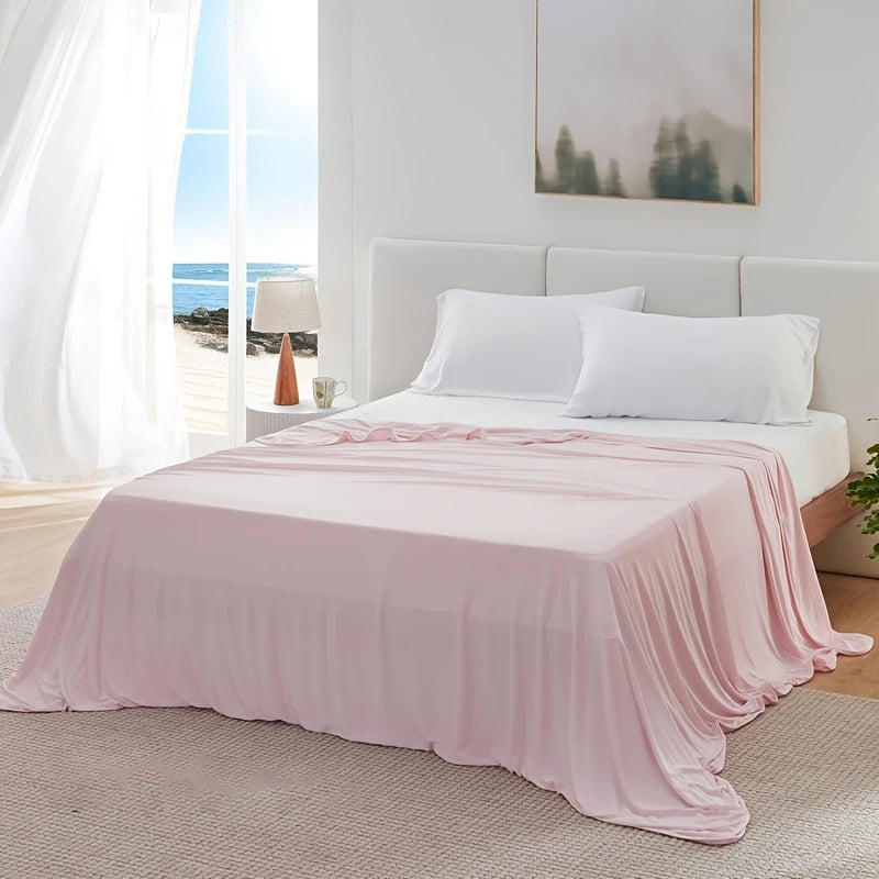 A pink ice silk blanket is draped over a white bed in a bright room with a view of the ocean.