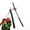 A replica Demon Slayer mini katana sword with a black handle and red guard, next to an anime figure.