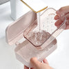 A hand is pouring water into a transparent soap dish with a drainage tray, which is part of a pink bathroom accessory.