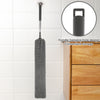 A gray microfiber duster with a handle is shown hanging on a tile, next to a wooden drawer.