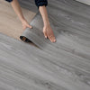 Hands are unrolling a roll of gray wood grain wallpaper onto a floor.