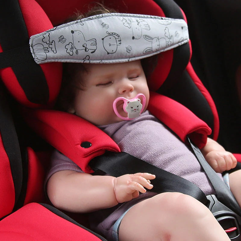 A baby is resting in a red car seat with a head and neck support pillow and safety strap.
