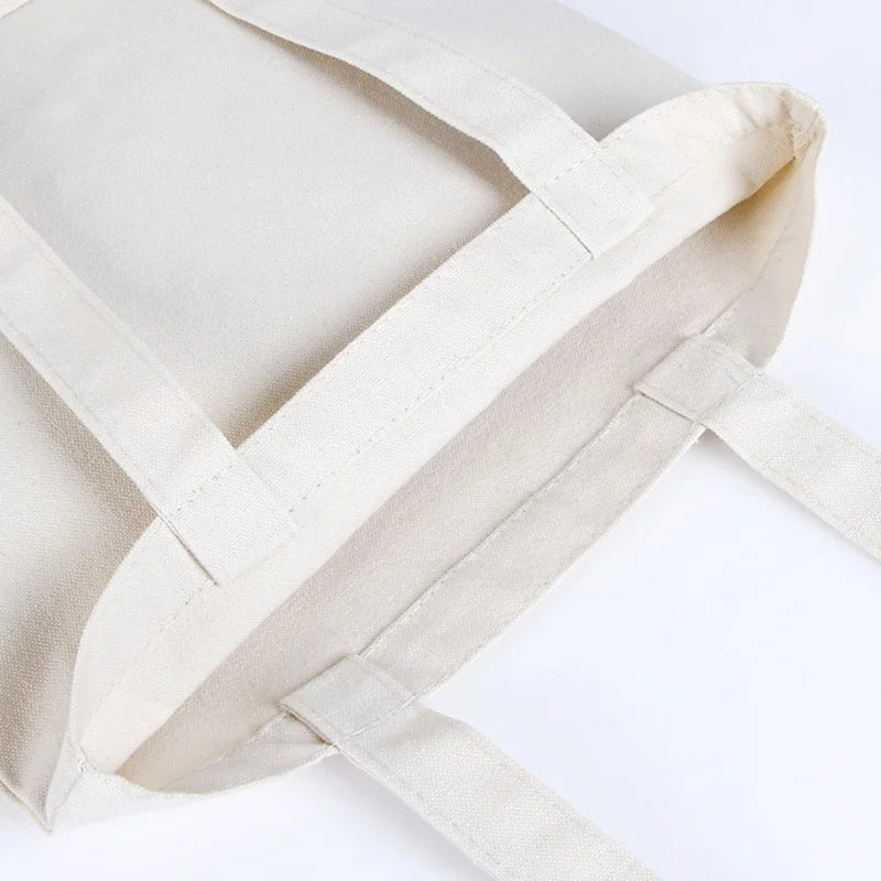 A light beige reusable canvas shopping tote bag with a foldable design shown from above.