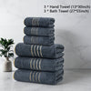A stack of three dark gray hand towels and three bath towels with gold stripes on a white marble surface.