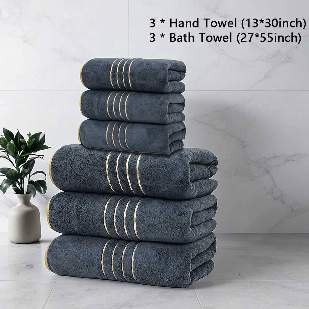 A stack of three dark gray hand towels and three bath towels with gold stripes on a white marble surface.