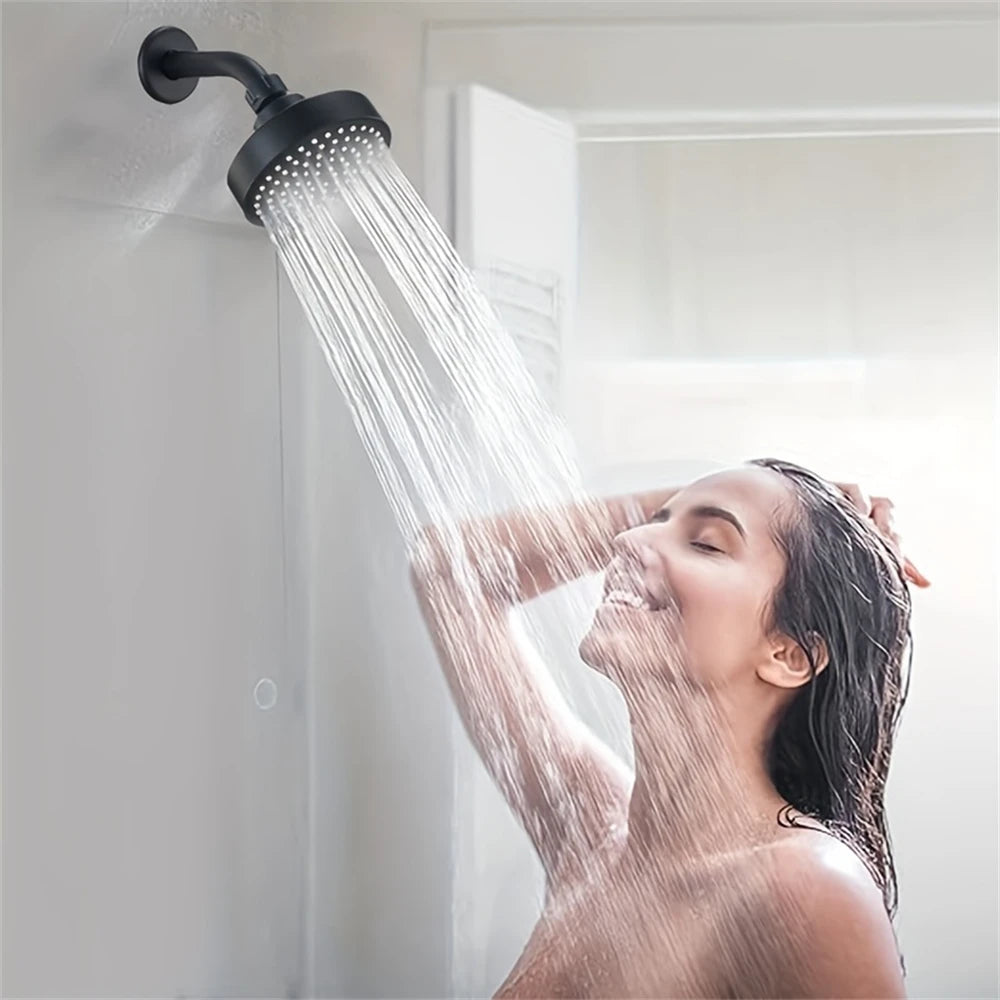 A woman is showering under a matte black shower head, with water streaming down her hair and face.