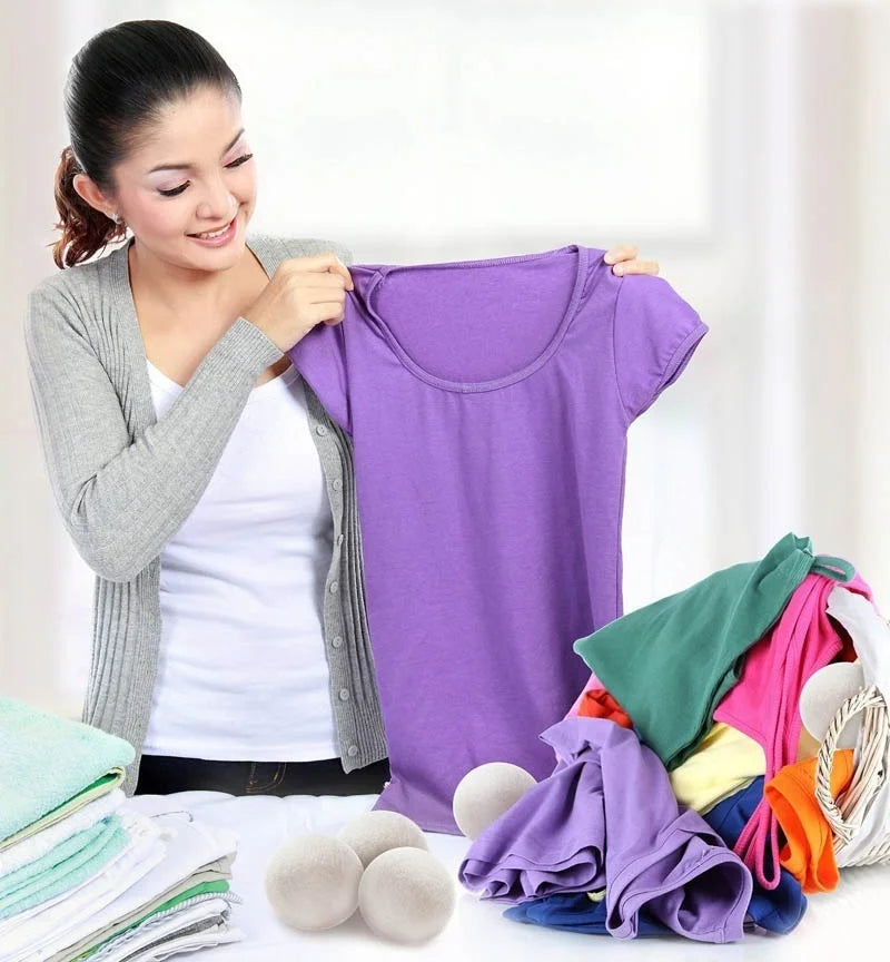 A woman holds up a purple natural wool dryer ball garment while surrounded by other colored fabric and dryer balls.