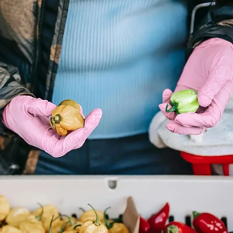 Pink nitrile gloves holding a green bell pepper in a kitchen setting