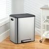 A stainless steel dual compartment step trash can with a black soft-close lid sitting on a wooden floor.