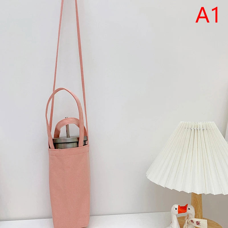 A pink canvas crossbody bag hanging on a wall next to a white lamp.