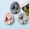 Three plush rabbit hot water bottles in shades of gray and pink resting on a light blue surface.