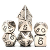 A set of seven metal polyhedral dice featuring a dragon font design, including a tetrahedron and a cube.