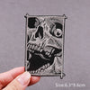 A black embroidered skull horror patch with intricate details is held by a hand.