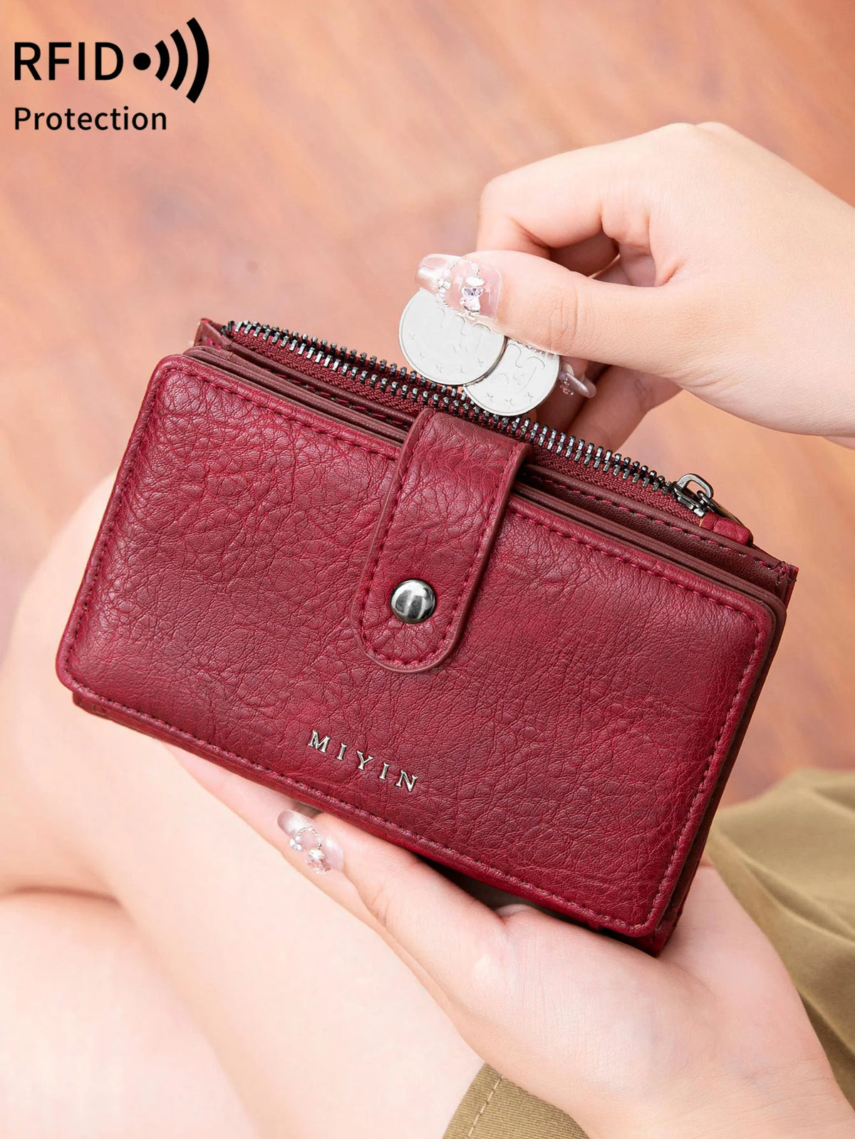 Une main tient un porte-monnaie plié en cuir marron anti-RFID avec une fermeture éclair argentée et une étiquette métallique.