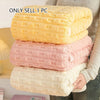 A stack of three coral and white velvet bath towels is shown next to a person's hand.