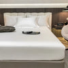 Juego de sábanas ajustadas de algodón de lujo sobre una cama blanca con varias almohadas y una bandeja oscura.