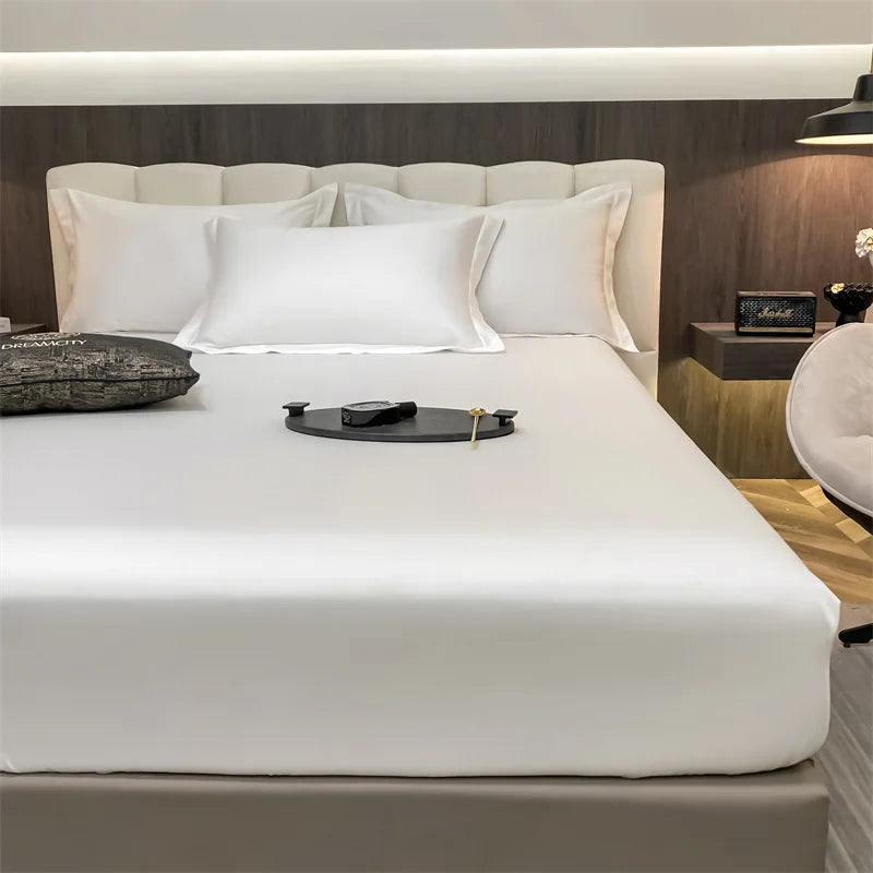 Juego de sábanas ajustadas de algodón de lujo sobre una cama blanca con varias almohadas y una bandeja oscura.