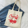 A cream canvas tote bag featuring a graphic design of cherries and the text Delicious Cherries.