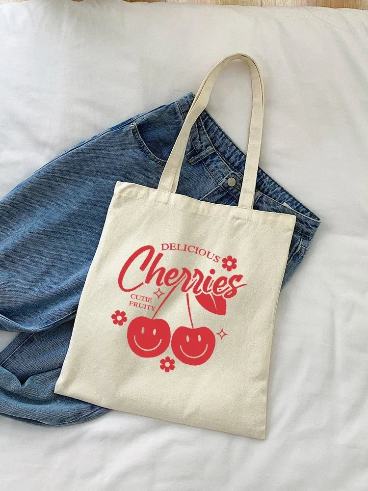 A cream canvas tote bag featuring a graphic design of cherries and the text Delicious Cherries.