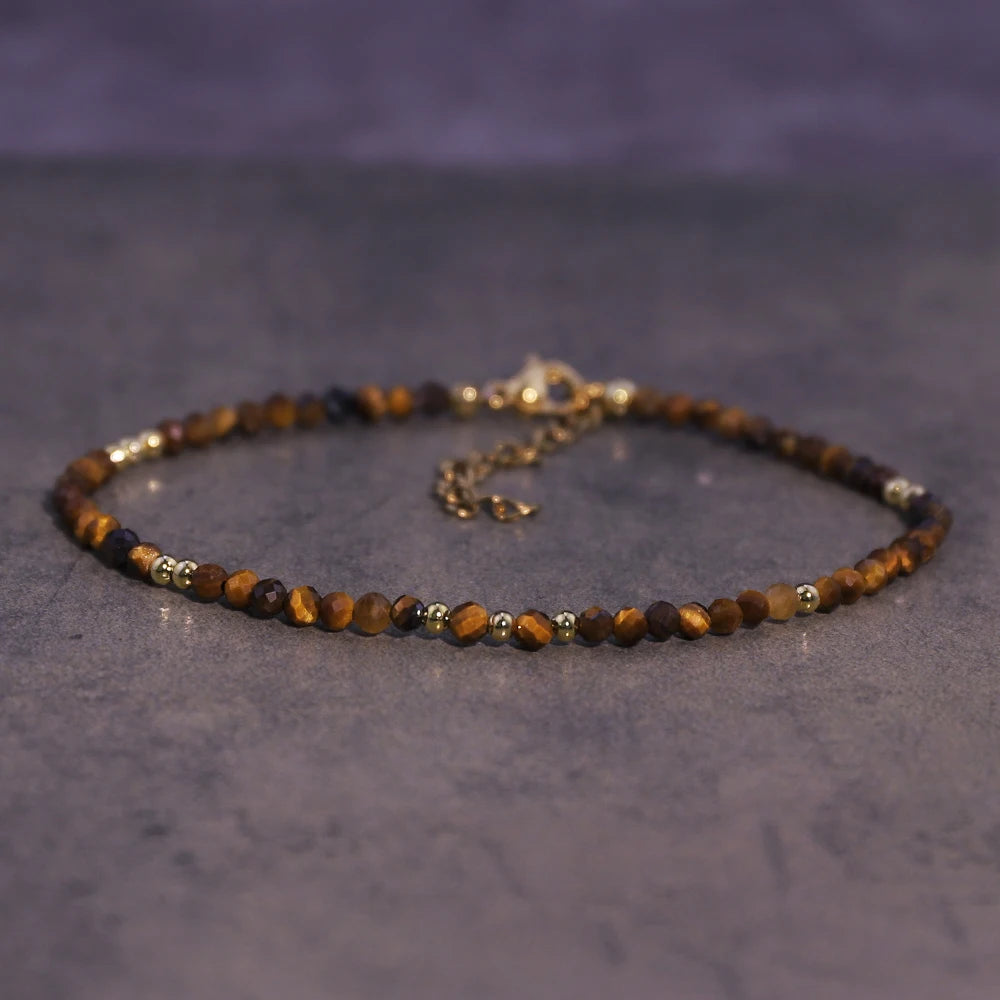 A brown natural crystal beaded bracelet with gold accents is laid on a dark gray surface.