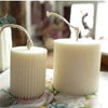 Two white pillar candles with natural twine wicks sit on a floral surface.