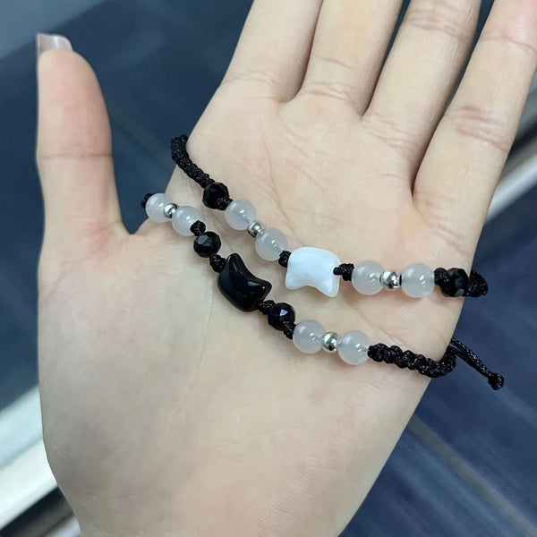 A bracelet set featuring small white moonstone and black obsidian beads on a black cord worn on a hand.