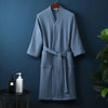A light blue waffle knit robe hanging on a dark blue wall.
