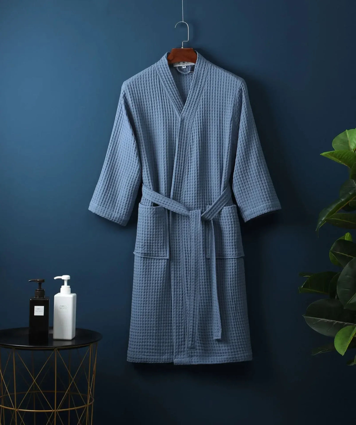 A light blue waffle knit robe hanging on a dark blue wall.