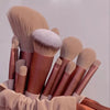 A collection of thirteen makeup brushes in various shades and sizes displayed in a brown travel bag.
