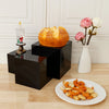 A golden baked loaf of bread sits on a black acrylic display riser next to a white candle and pink roses.