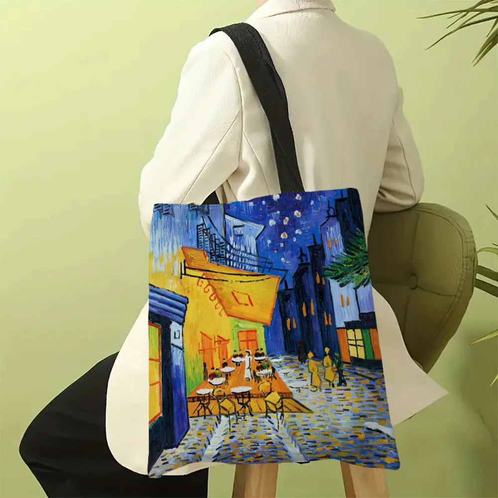 A canvas tote bag featuring a Van Gogh style painting of a street scene with yellow and blue buildings and figures.