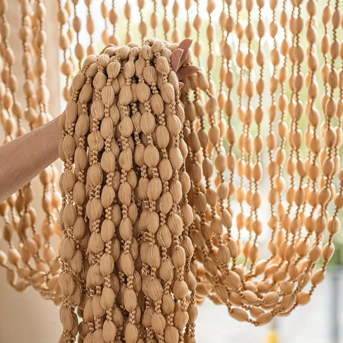 A close-up of a beige bohemian tassel curtain with light wood lanterns hanging down.