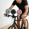 A man is riding a bicycle with a flexible octopus USB fan mounted on the handlebars.