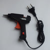 A black hot melt glue gun with a stand and power cord is shown on a white surface.