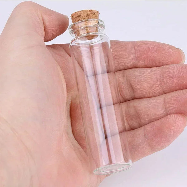 A hand holds a clear glass bottle with a cork stopper, used for DIY crafts and gifting.