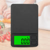 A black mini digital scale with a green display showing 0.00, shown against a blurred background of fresh produce.