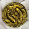 Runde, goldfarbene antike chinesische Koi-Glücksmünze mit filigranen Designs in der Hand.