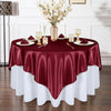 A burgundy satin tablecloth is draped over a round table set for an elegant dining event.