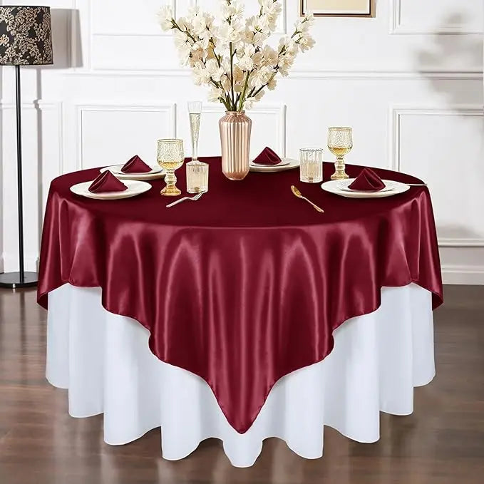 A burgundy satin tablecloth is draped over a round table set for an elegant dining event.