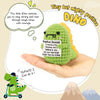 A hand holds a green crochet dinosaur plush toy with yellow accents, illustrating positive encouragement.