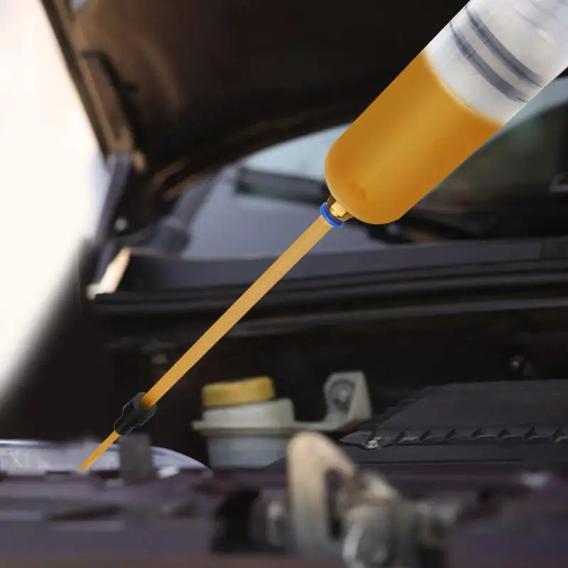 A close-up of a manual fluid extractor and injection pump with a long yellow hose being used on a vehicle component.