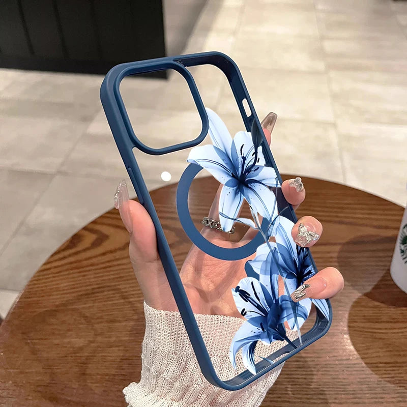 A hand holds a blue magnetic phone case featuring a white and blue lily design on a wooden table.