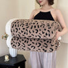 A woman models a leopard print plush jacquard throw blanket draped over her arm.