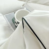 A white duvet cover set with a folded white blanket and a white mug on a bed.