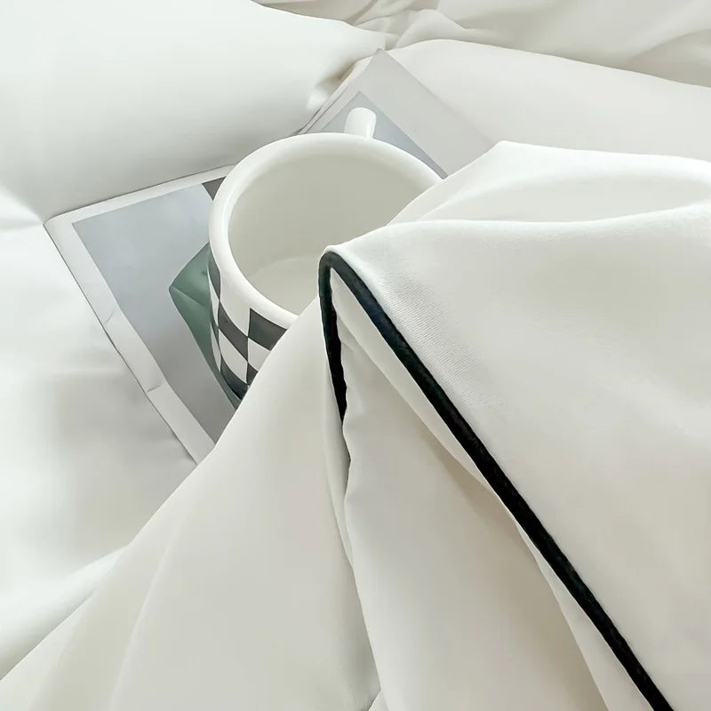 A white duvet cover set with a folded white blanket and a white mug on a bed.
