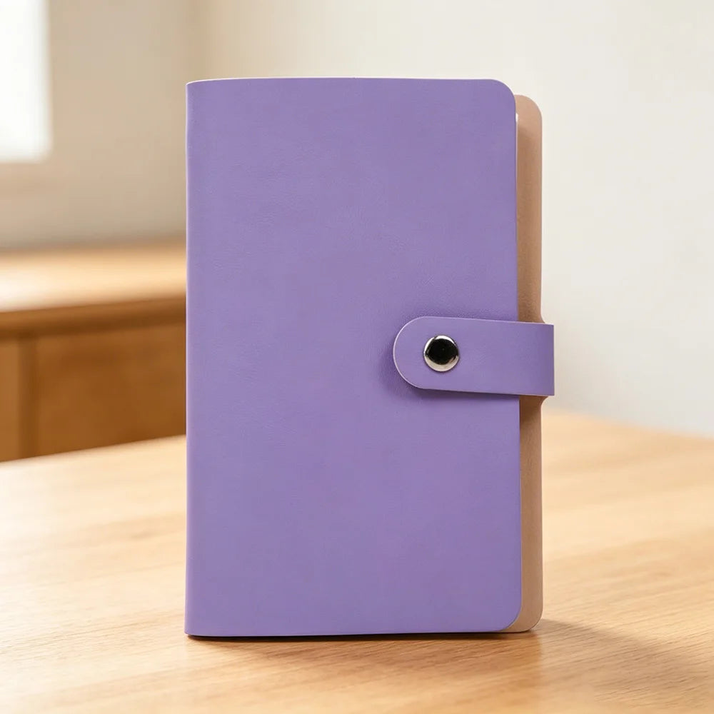 A purple 100-slot cash organizer binder with a snap closure and a light brown cover, resting on a wooden surface.